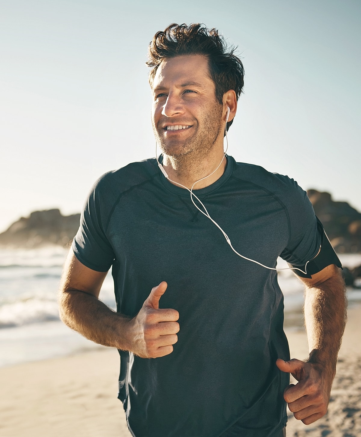 Man jogging on beach with headphones.