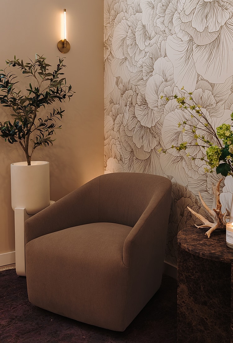 Cozy chair beside floral wallpaper and plants.