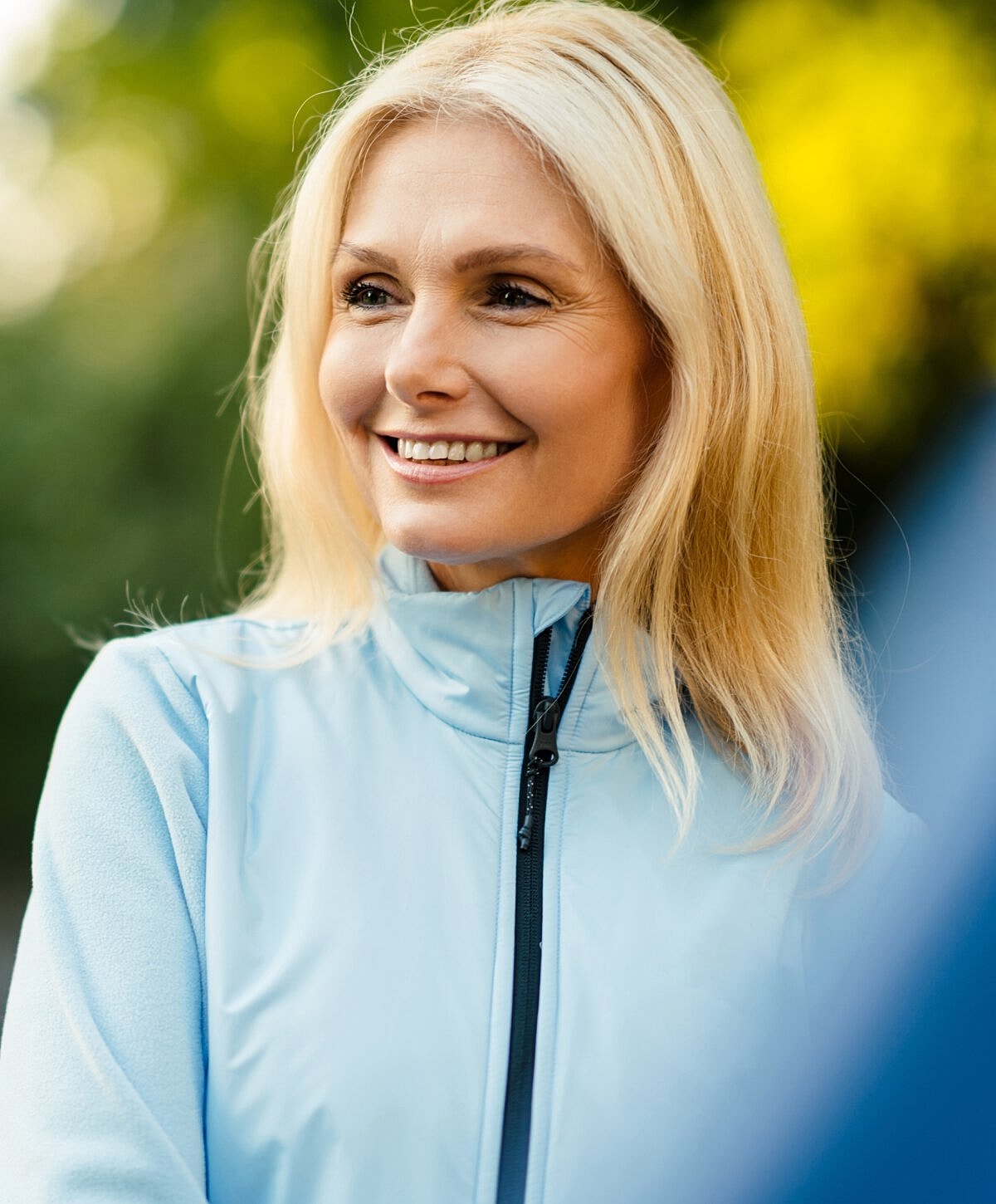 Smiling woman in light blue jacket outdoors.