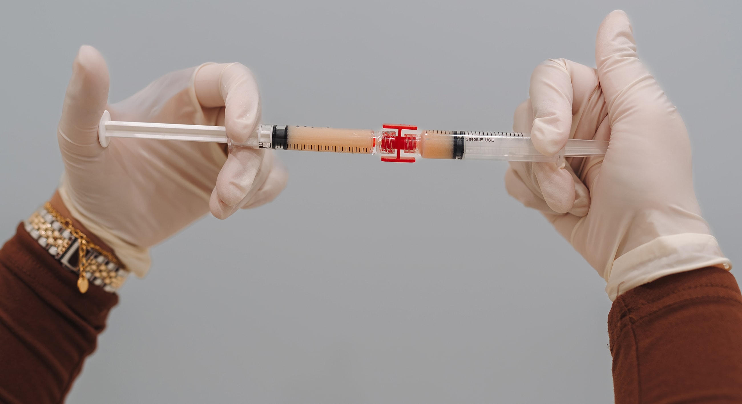 Hands holding a syringe with a red safety cap.